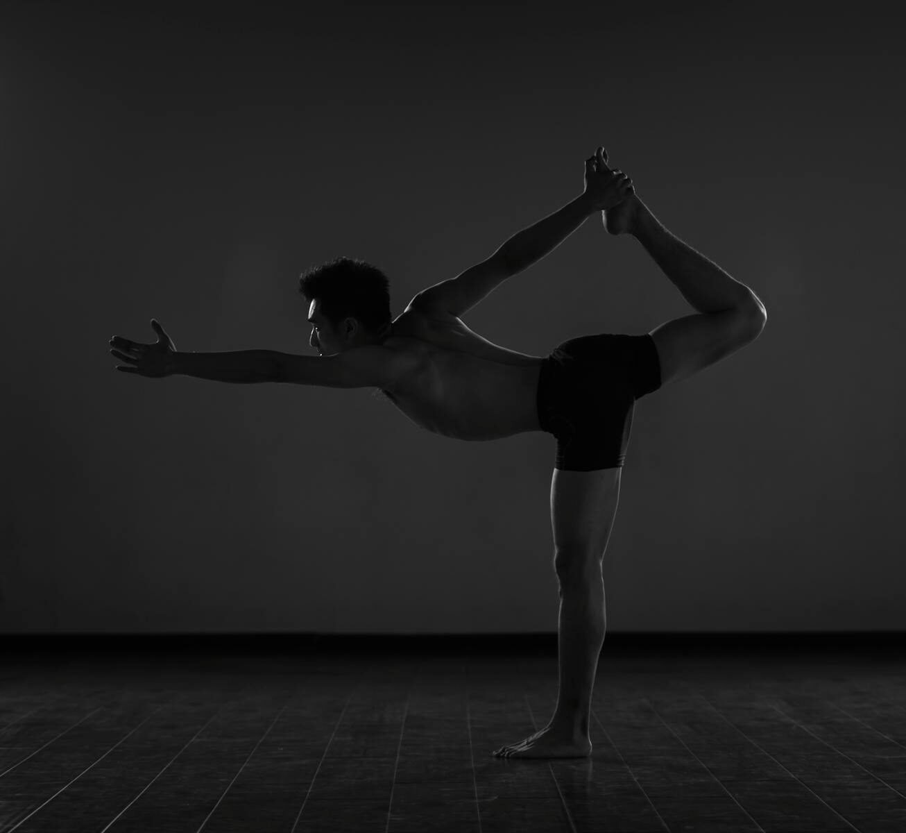 A shirtless man balances in a yoga pose, creating a striking silhouette.