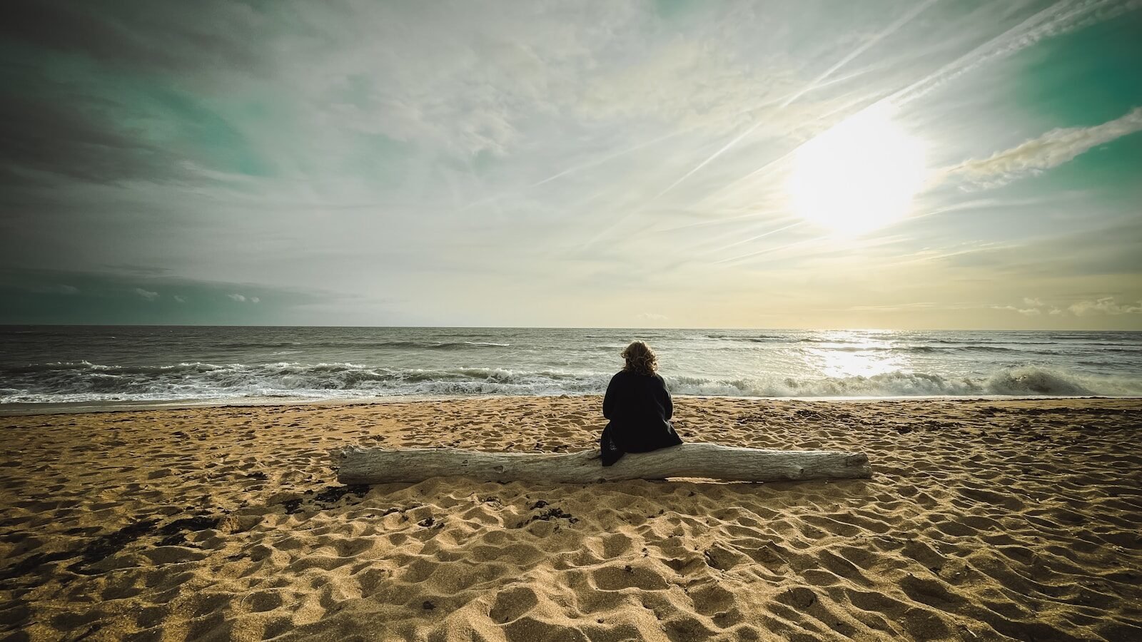 Person sitting on log facing the ocean waves.