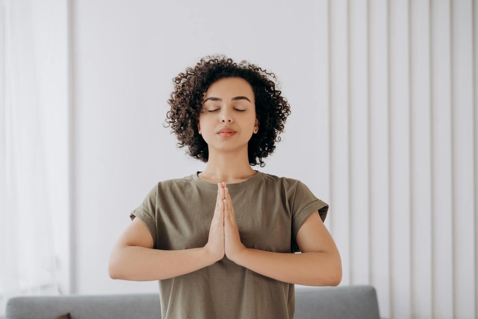 Young woman with curly hair meditates indoors, embracing tranquility and mindfulness.